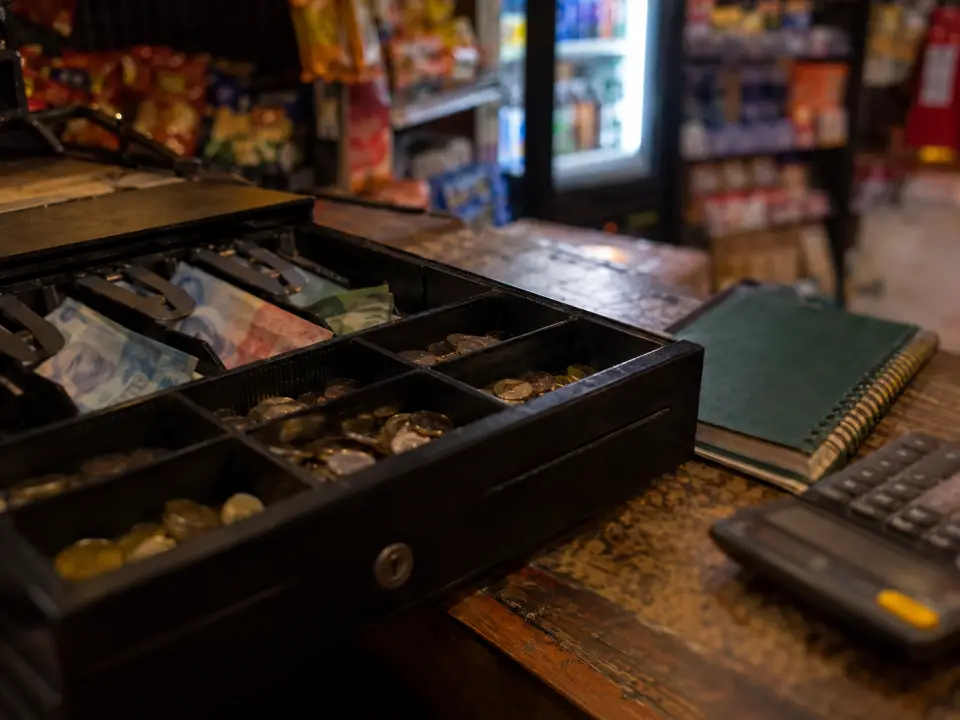 Gaveta de caja abierta con billetes desenfocados, cuaderno y calculadora al cierre del día