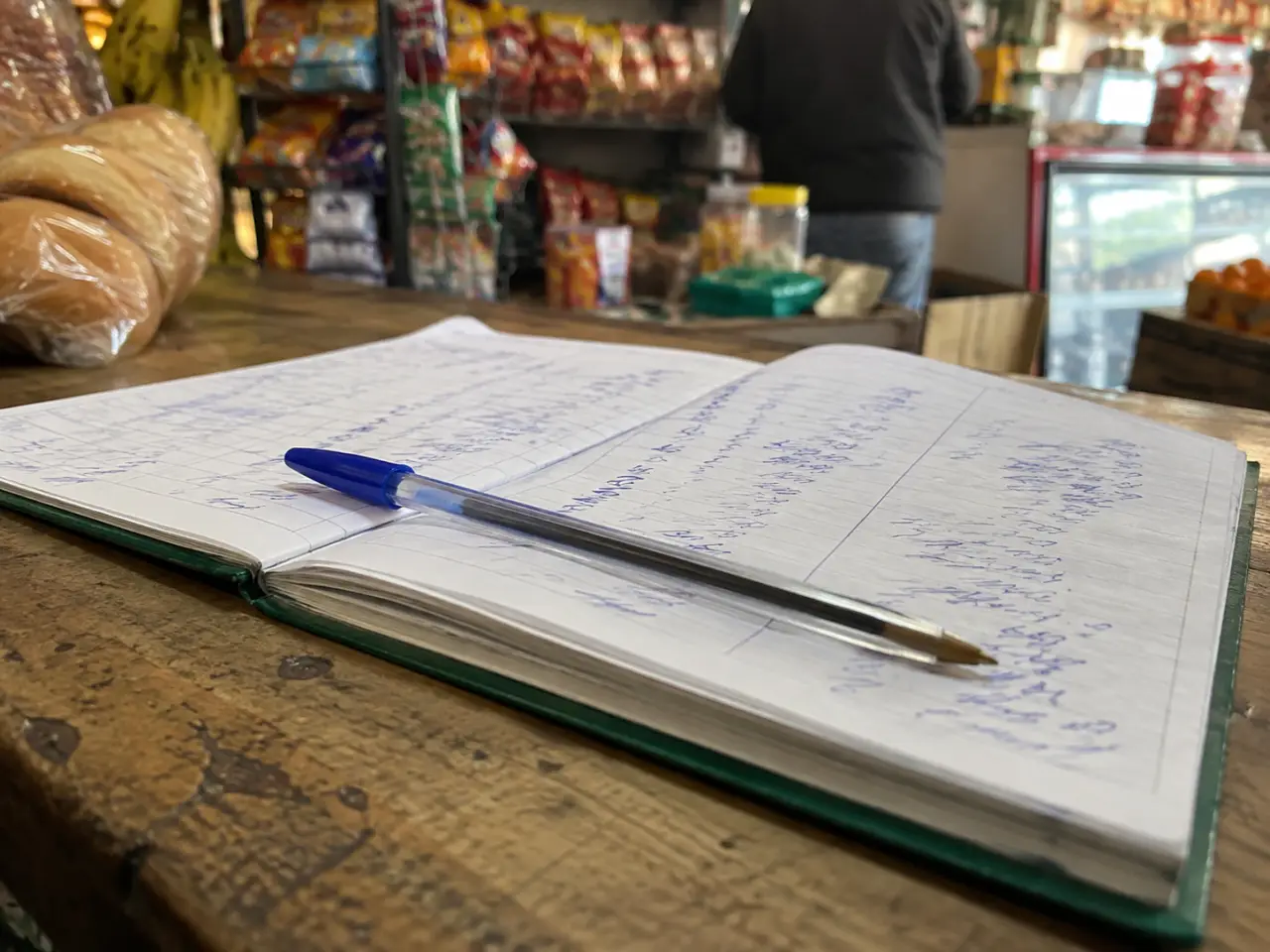Cuaderno escolar abierto con columnas del fiado escritas a mano sobre un mostrador de madera