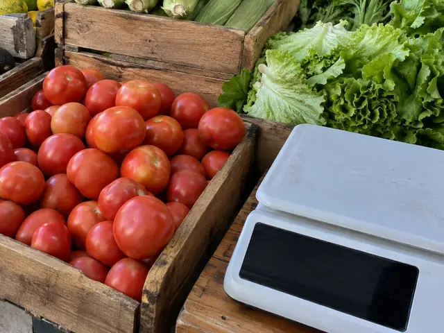 Balanza blanca de mesón junto a un cajón de tomates y lechugas en una verdulería